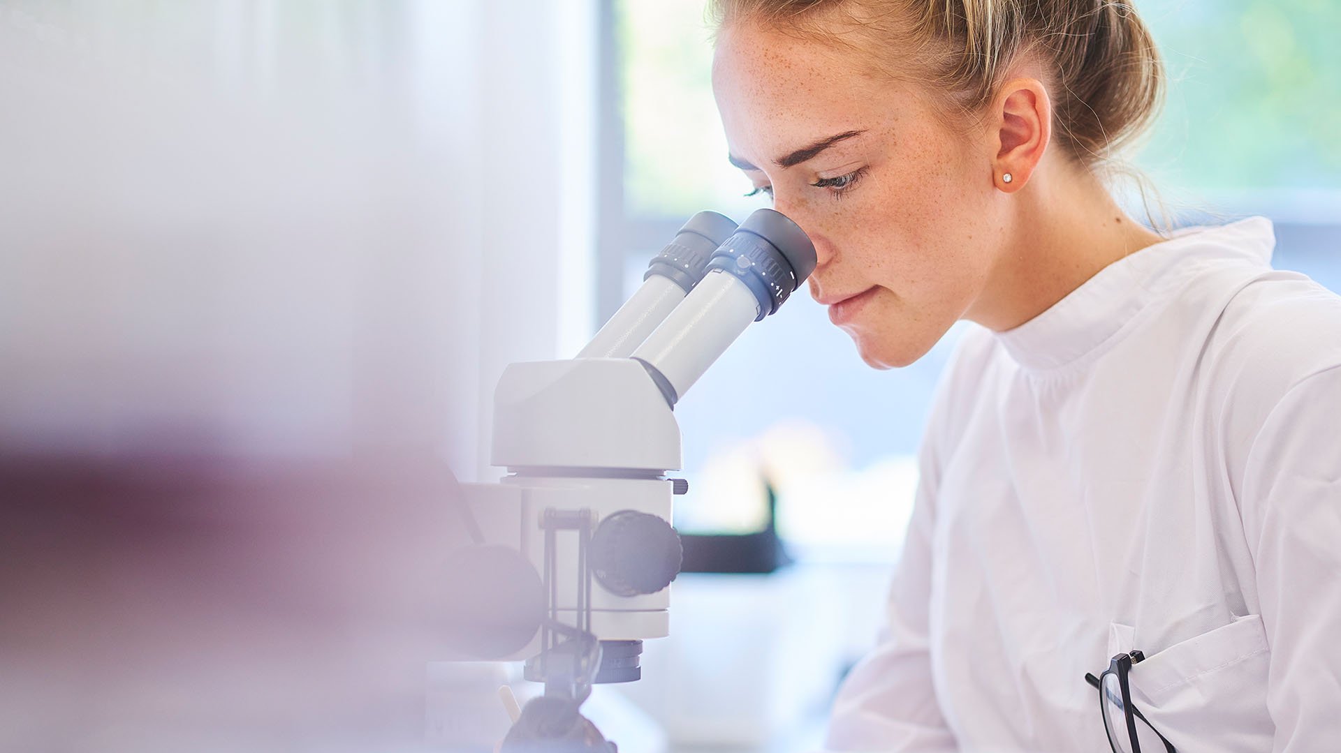 Schülerin in einem weißen Pullover schaut durch ein Mikroskop
