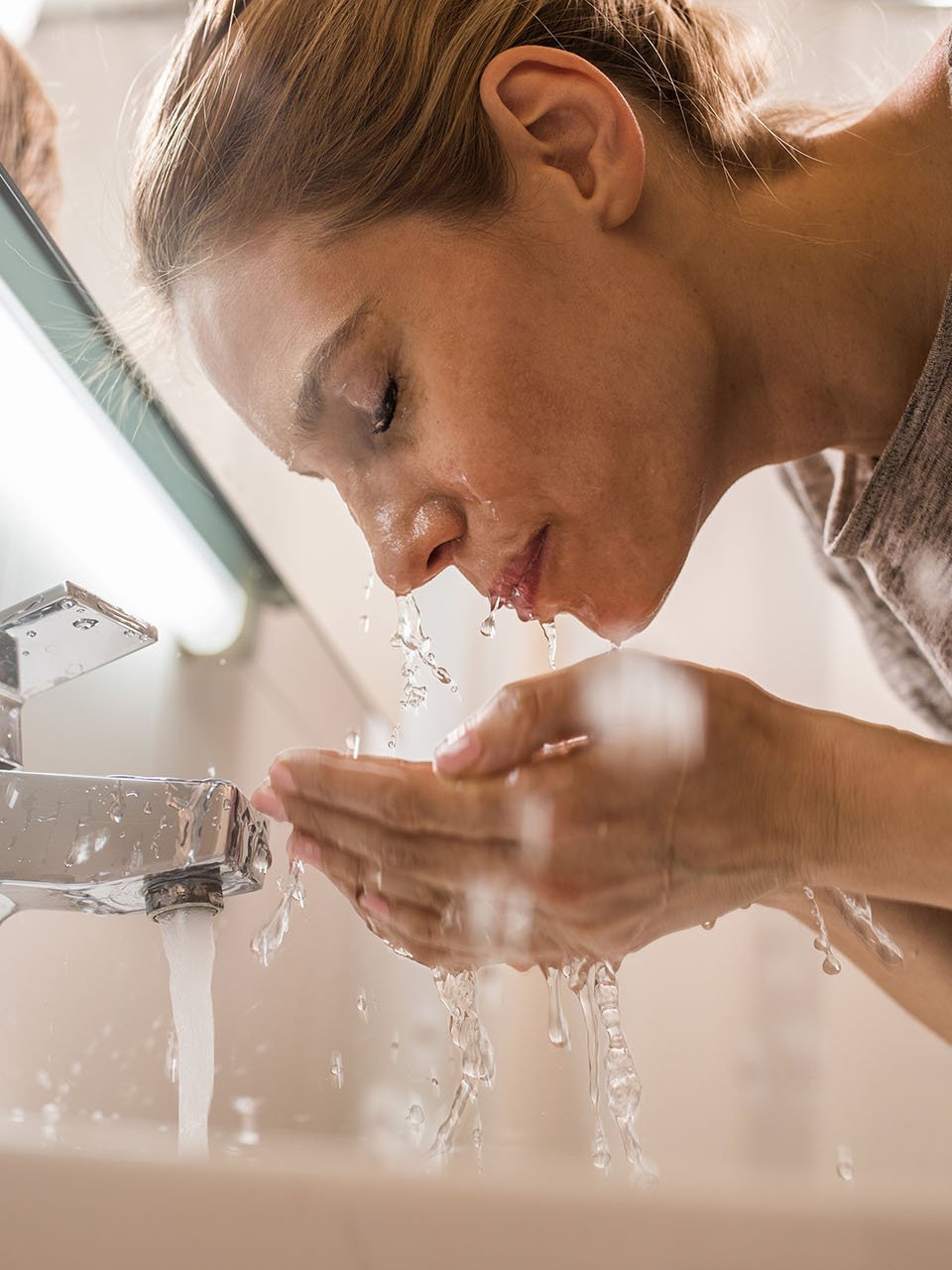 Frau wäscht sich über dem Waschbecken das Gesicht