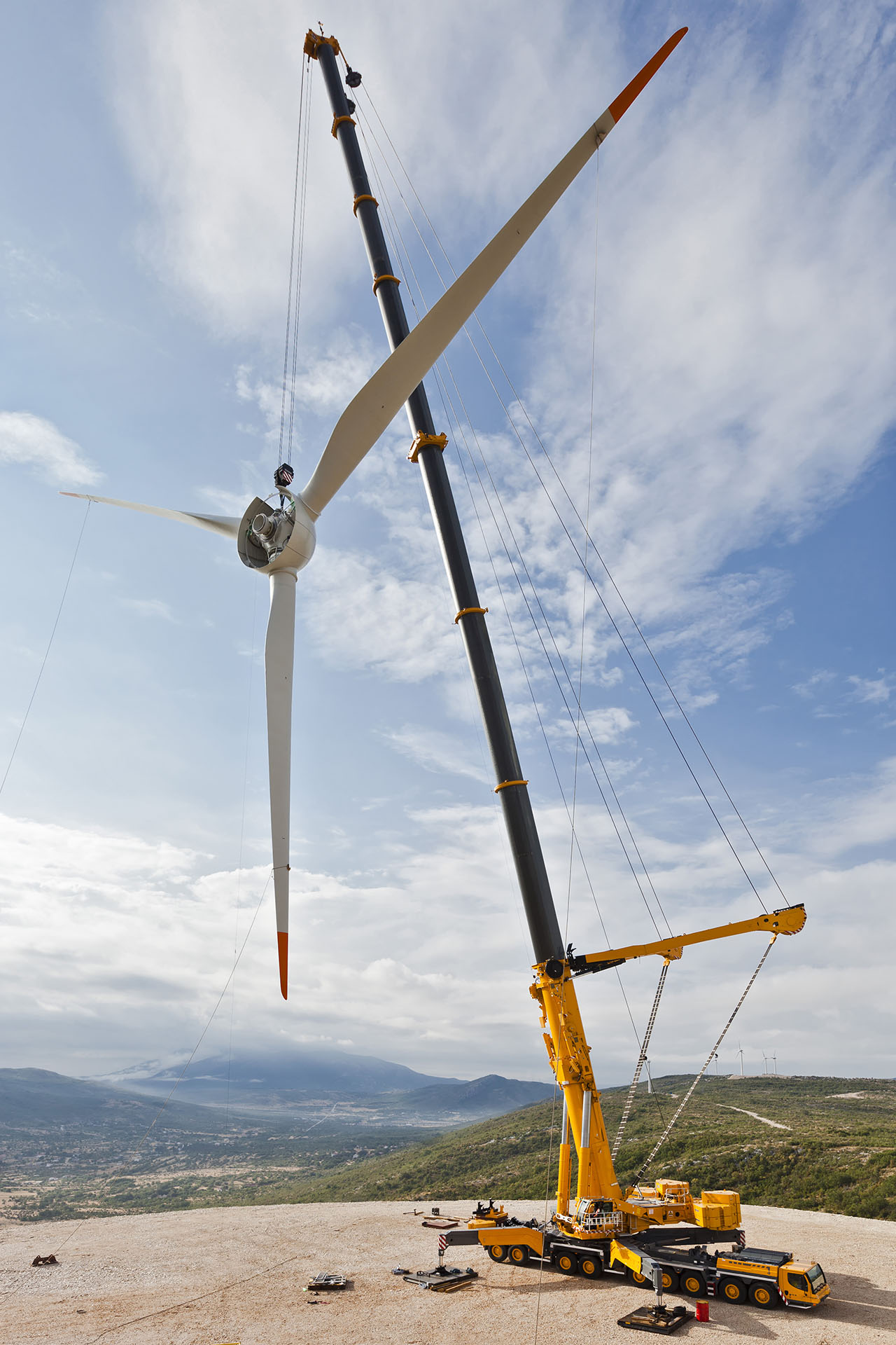 Une grue télescopique jaune soulève les pales d'une éolienne