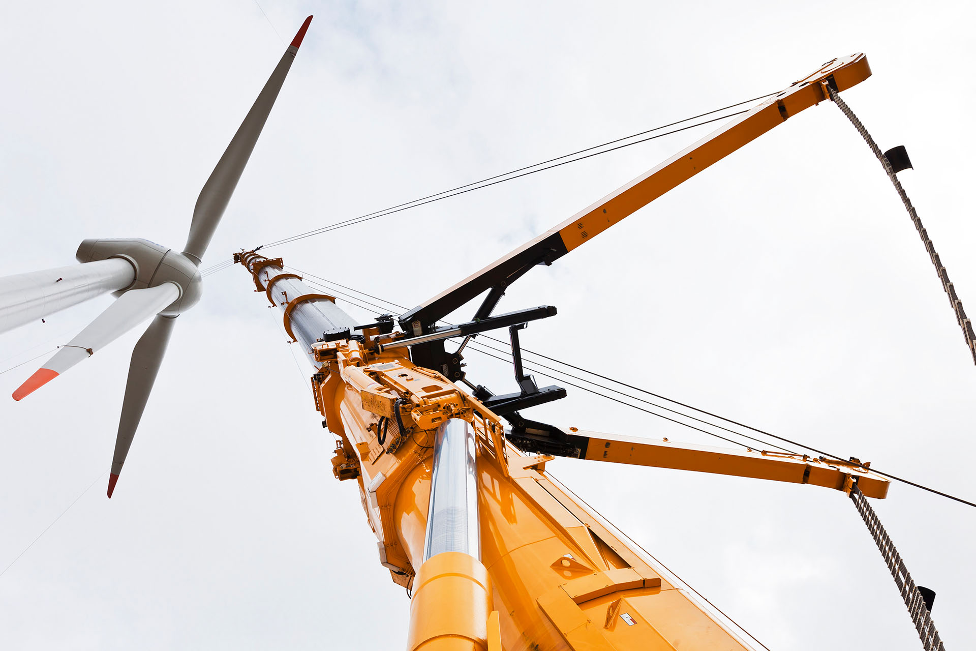 Une grue télescopique jaune soulève une éolienne dans les airs