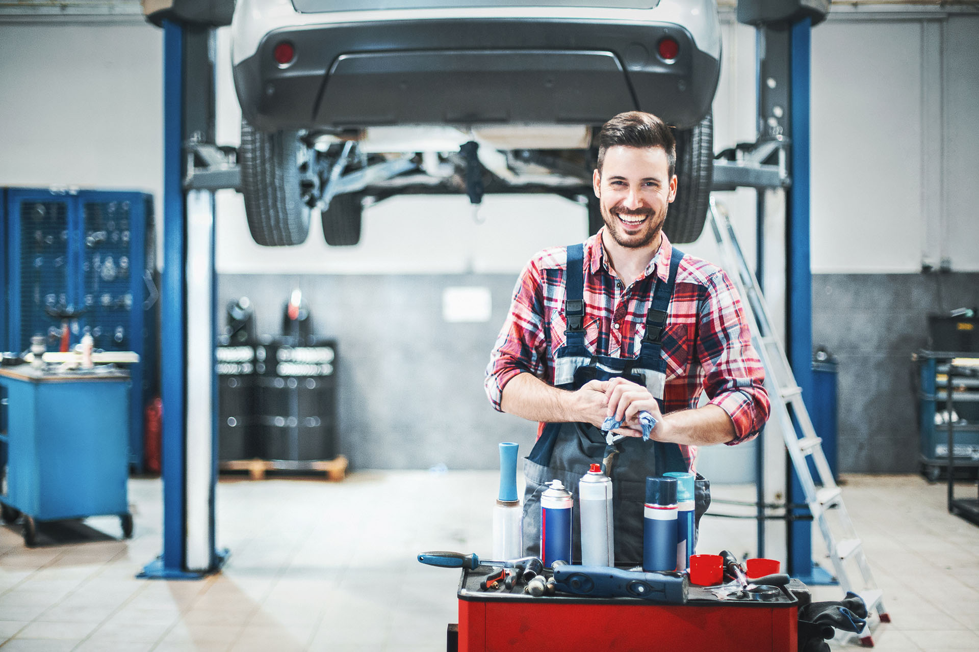 Mecánico de coches en el taller con el coche en la plataforma elevadora