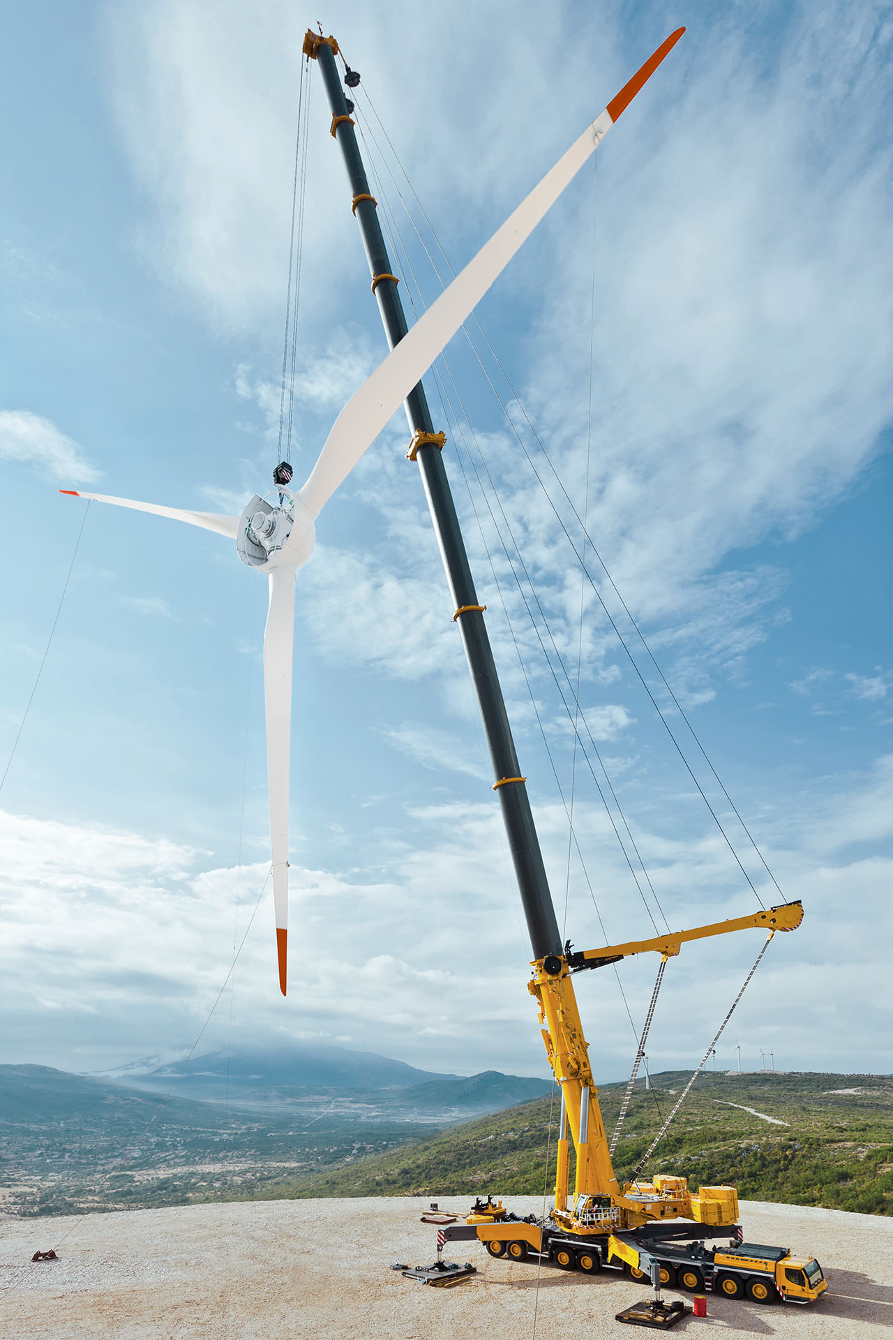 Une grue télescopique jaune soulève les pales d'une éolienne