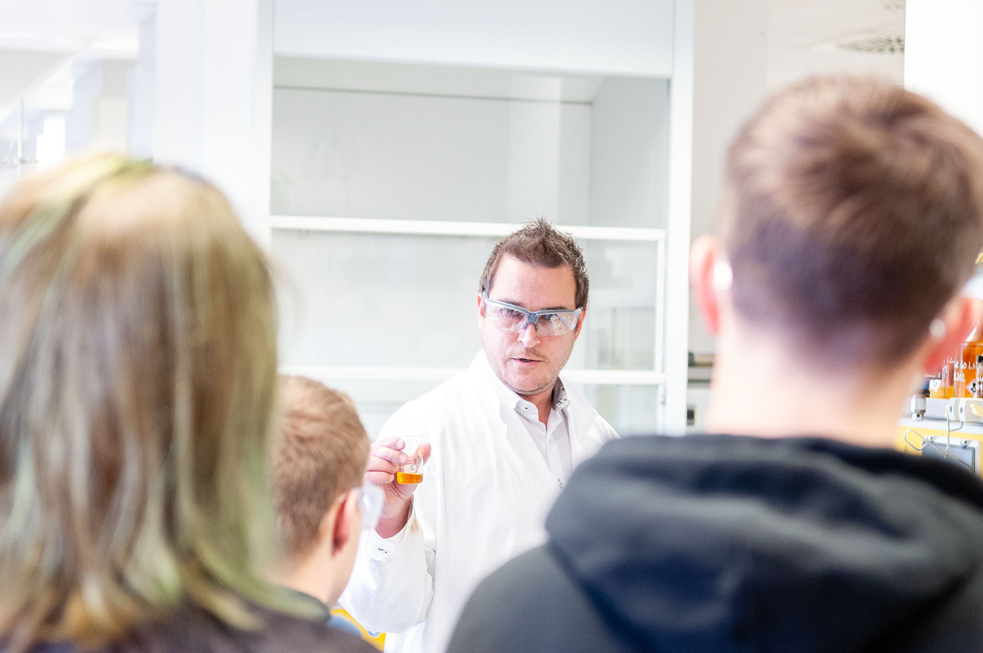 Mann mit Schutzbrille erklärt Schülern Chemie