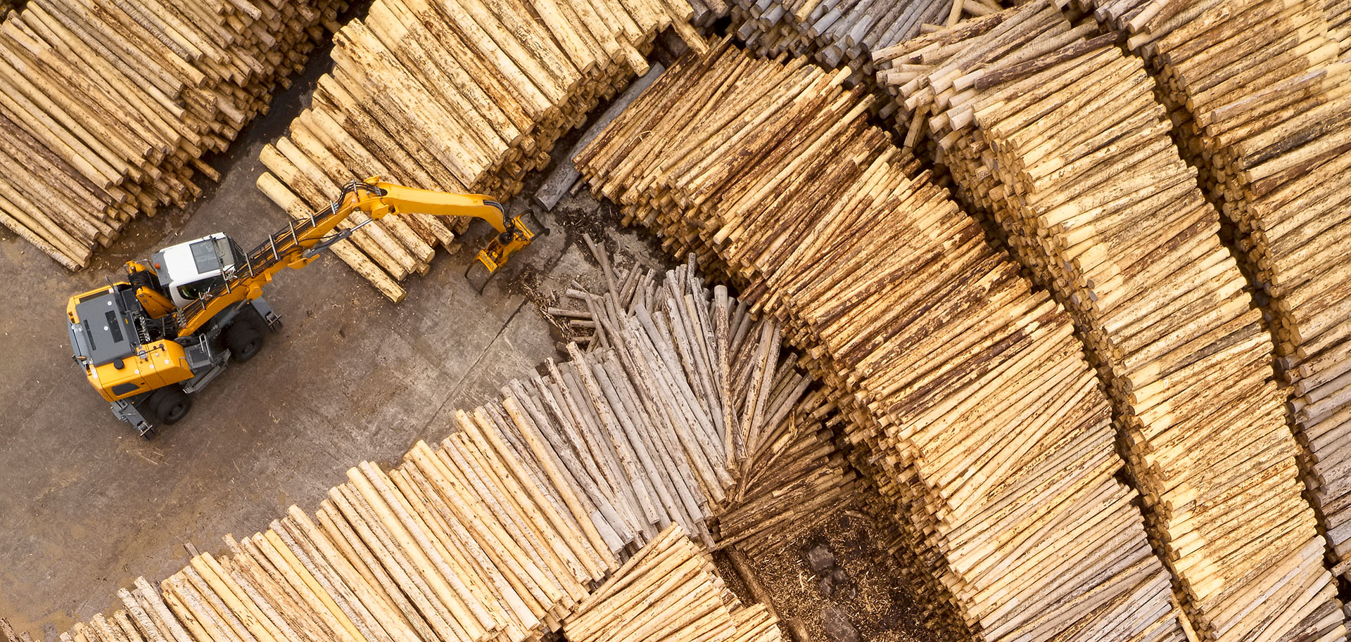 Yellow excavator moves stacked wood 